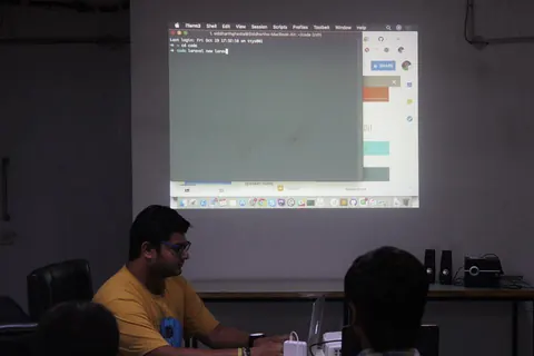 A man at a laptop runs a terminal demo, with a laravel new command projected on the screen for attendees.