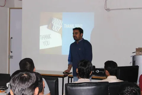 A man stands before a projected thank you slide as he wraps up his talk in front of seated attendees.