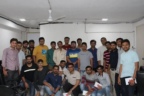 About twenty-five men pose for a group photo in an office room, a few holding white envelopes.