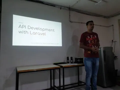 A man stands beside a projected slide titled API Development with Laravel in a dim room.