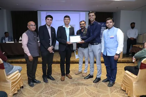 A group of men in formal attire pose in a banquet hall while two of them hold a framed award plaque together.