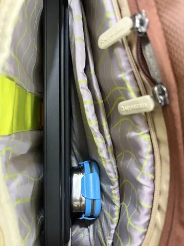 Close-up inside a bag showing a laptop lid propped slightly open by a blue clip for airflow