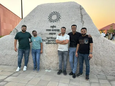 Five men pose before the rock of the National Salt Satyagrah Memorial at sunset.