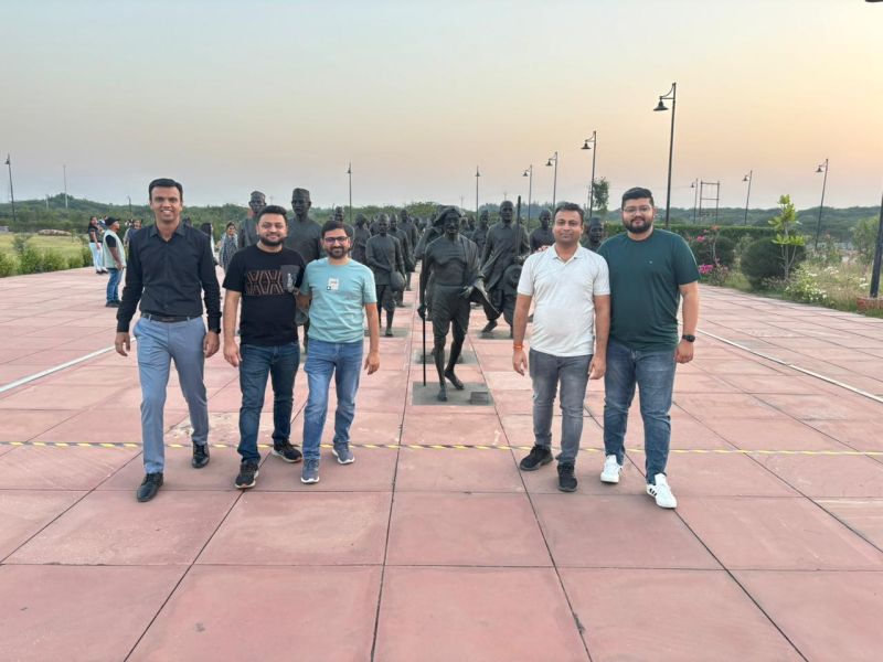 Five men stand on a plaza among bronze statues of salt marchers at dusk.