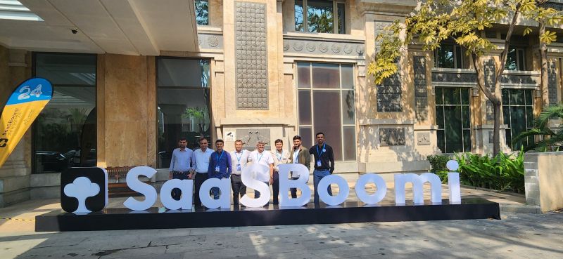 Group of men standing outdoors behind large SaaSBoomi letters outside a venue entrance.
