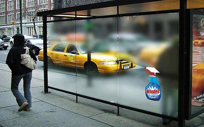 Bus shelter glass looks smudged except where a Windex spray bottle graphic sits, a taxi blurred behind.