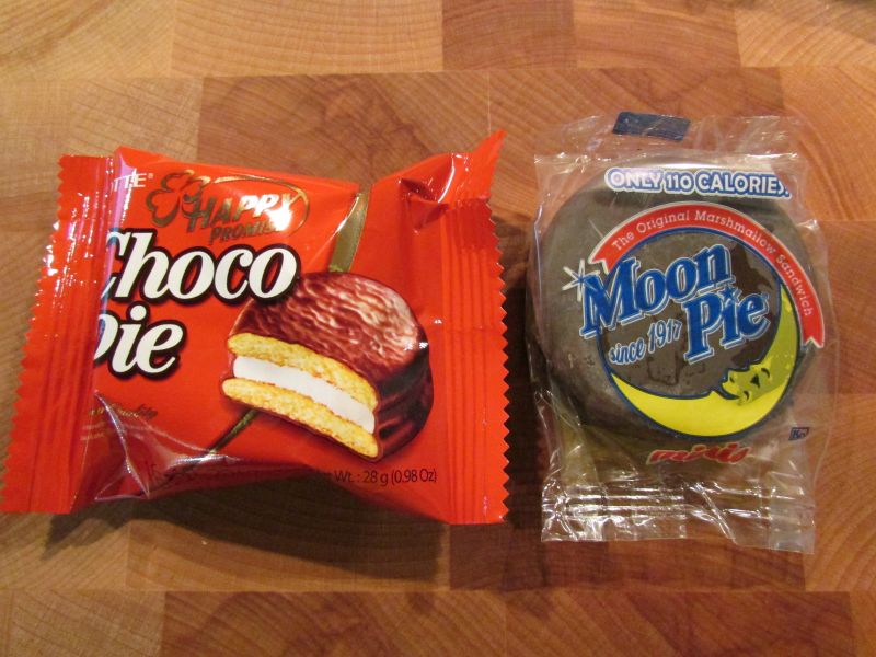 A Choco Pie in orange packaging beside a wrapped MoonPie on a wooden surface