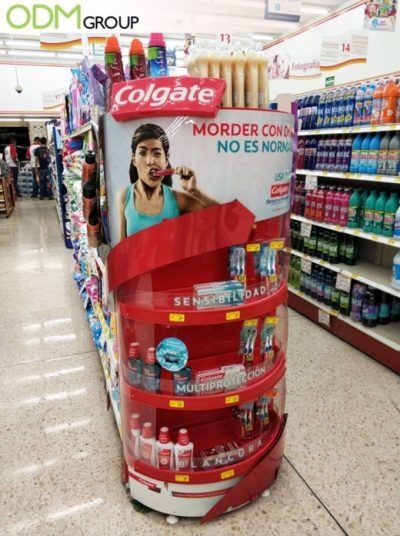 Red Colgate toothpaste endcap display with Spanish signage in a supermarket aisle.