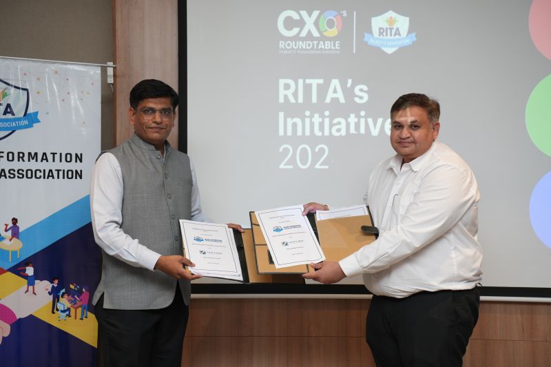 Two men hold framed mementoes in front of a screen reading CXO's Roundtable and RITA's Initiatives.