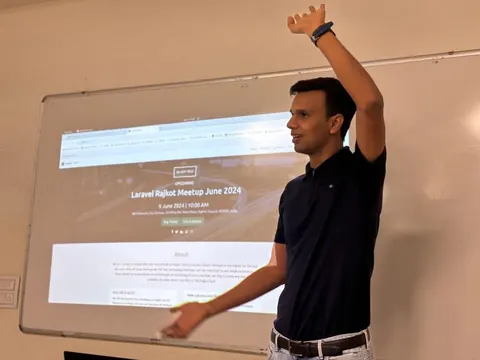 A man gestures beside a projector screen showing the Laravel Rajkot Meetup June 2024 event page dated 9 June.