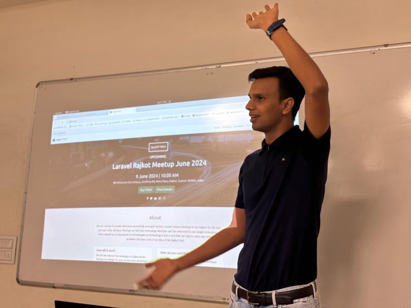 A man gestures beside a projector screen showing the Laravel Rajkot Meetup June 2024 event page dated 9 June.