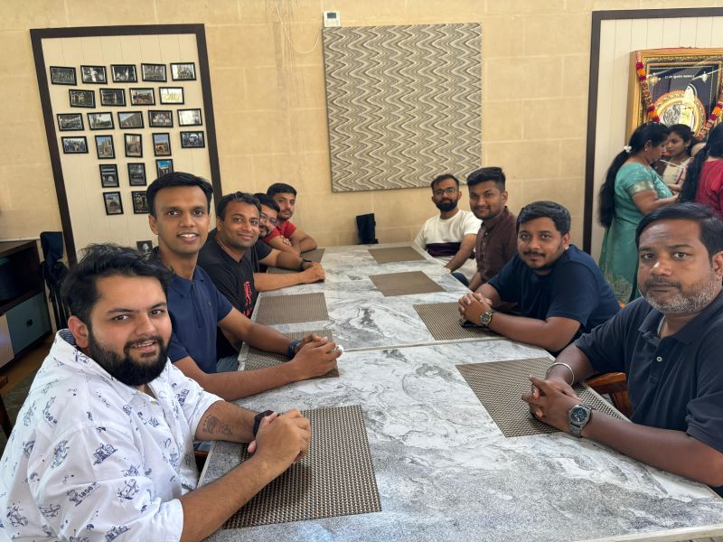 A group of men sits around a long marble table in a restaurant, smiling at the camera.