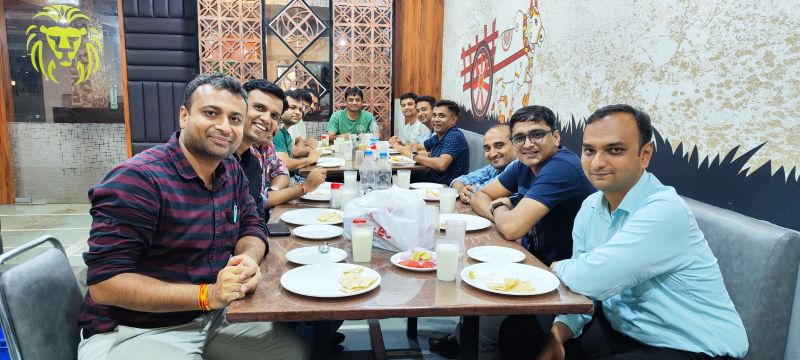 A group of men smile around a restaurant table set with plates of food, glasses and water bottles.