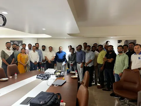 Group of about twenty-five professionals standing around a conference table in an office meeting room