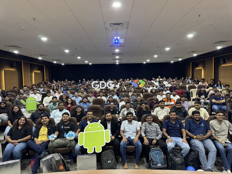 Large audience seated in an auditorium at a GDG Devfest event, with Android cutouts in the foreground.