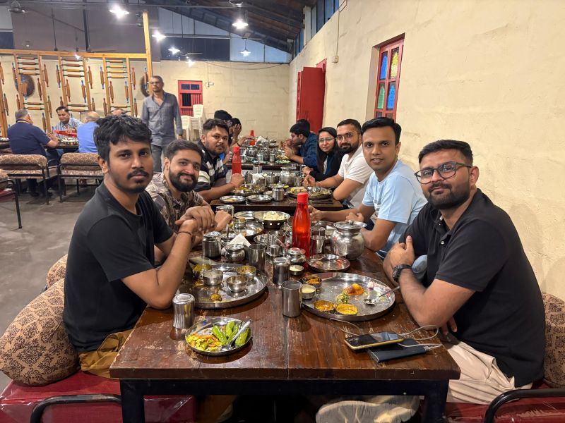Group of men sharing a meal around a restaurant table set with steel thali plates and glasses.