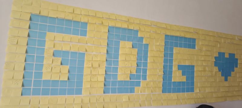Wall of yellow and blue sticky notes arranged to spell GDG with a heart.
