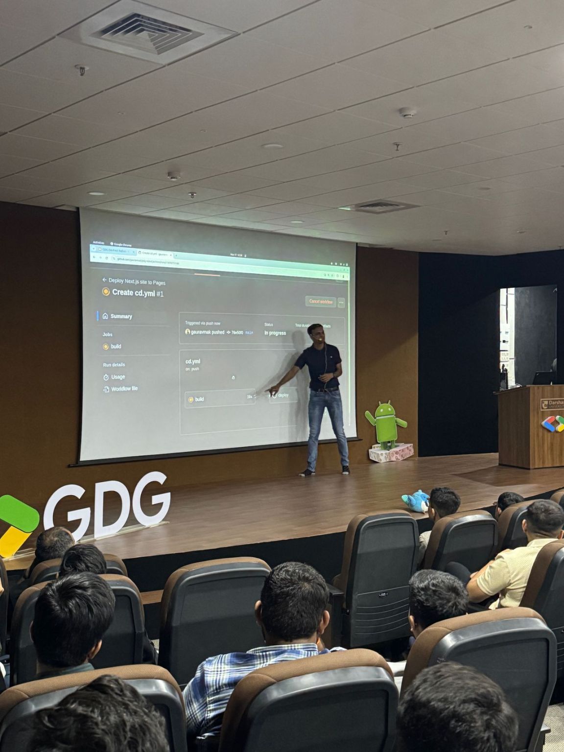 Gaurav points to a projected GitHub Actions workflow run while presenting to an auditorium audience.