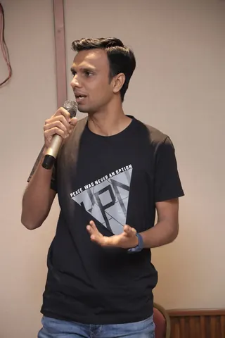 A man speaks into a microphone wearing a black T-shirt that reads Peace was never an option.