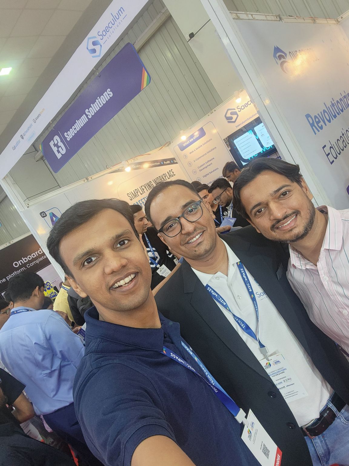 A man takes a selfie with two men at the Saeculum Solutions stall E3 at a technology expo.