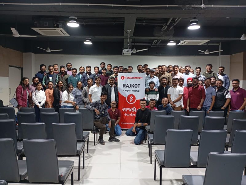Large group of meetup attendees posing in a seminar room with an IT Sales Community Rajkot banner.