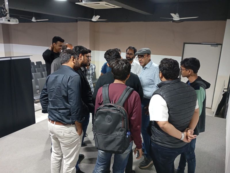 Group of men stand in a circle chatting in a seminar room during a break at a meetup.