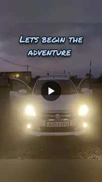White car with headlights on at dusk, doors open, under the words Lets begin the adventure.