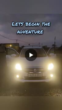 White car with headlights on at dusk, doors open, under the words Lets begin the adventure.