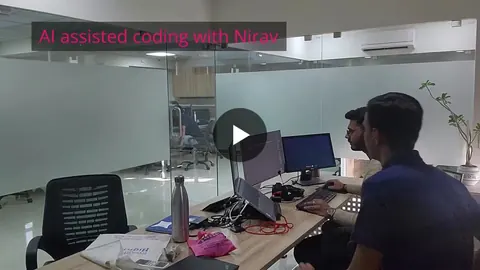 Two men at an office desk with monitors and a laptop, overlay reads 'AI assisted coding with Nirav'.