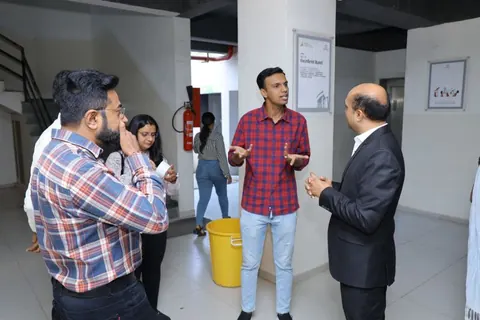 A group of attendees chats in a venue lobby as a man in a checked shirt gestures while talking to a man in a suit.