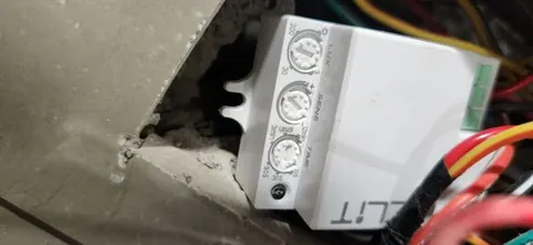 White motion sensor switch with three knobs labelled LUX, SENS and TIME, wired inside a rough wall opening.