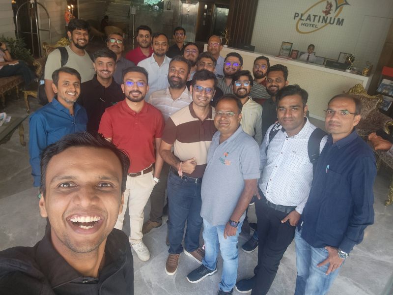 A smiling man takes a selfie with a large group of men in the Platinum Hotel lobby.