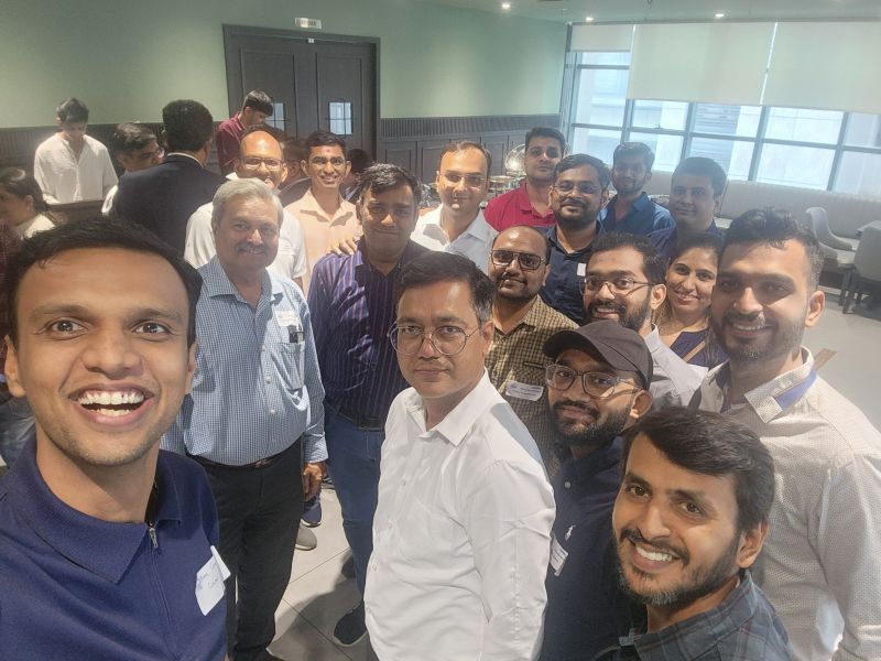 A man takes a group selfie with smiling attendees at an indoor networking event.