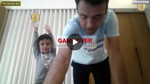 A man and a young child raise their arms playing a webcam coin-catching game that shows Game Over on screen.