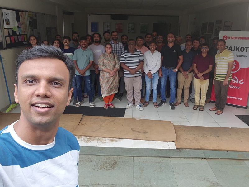 Man taking a selfie in front of a large group of attendees at a Rajkot IT sales community meetup.