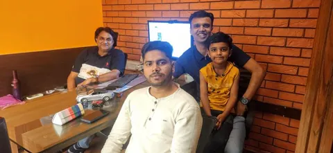 Four people, including a child in a yellow shirt, pose together in an office with model cars on the desk.