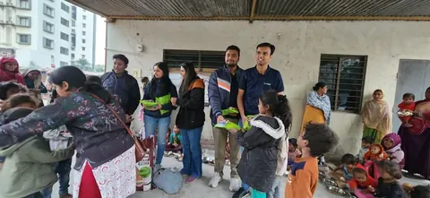 Adults hold green packets while children and families gather for a community meal during a donation drive.
