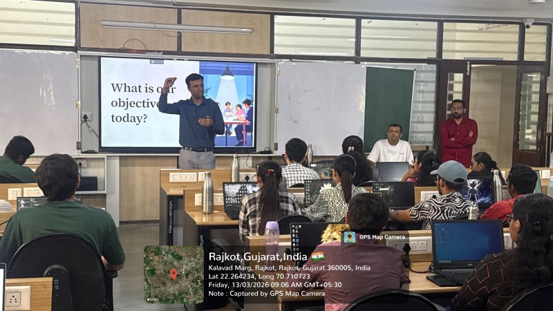 Presenter at a slide reading 'What is our objective today?' with students on laptops in a Rajkot classroom.