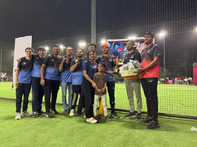 A group of players with medals, a trophy and a gift hamper pose together on the turf at night.
