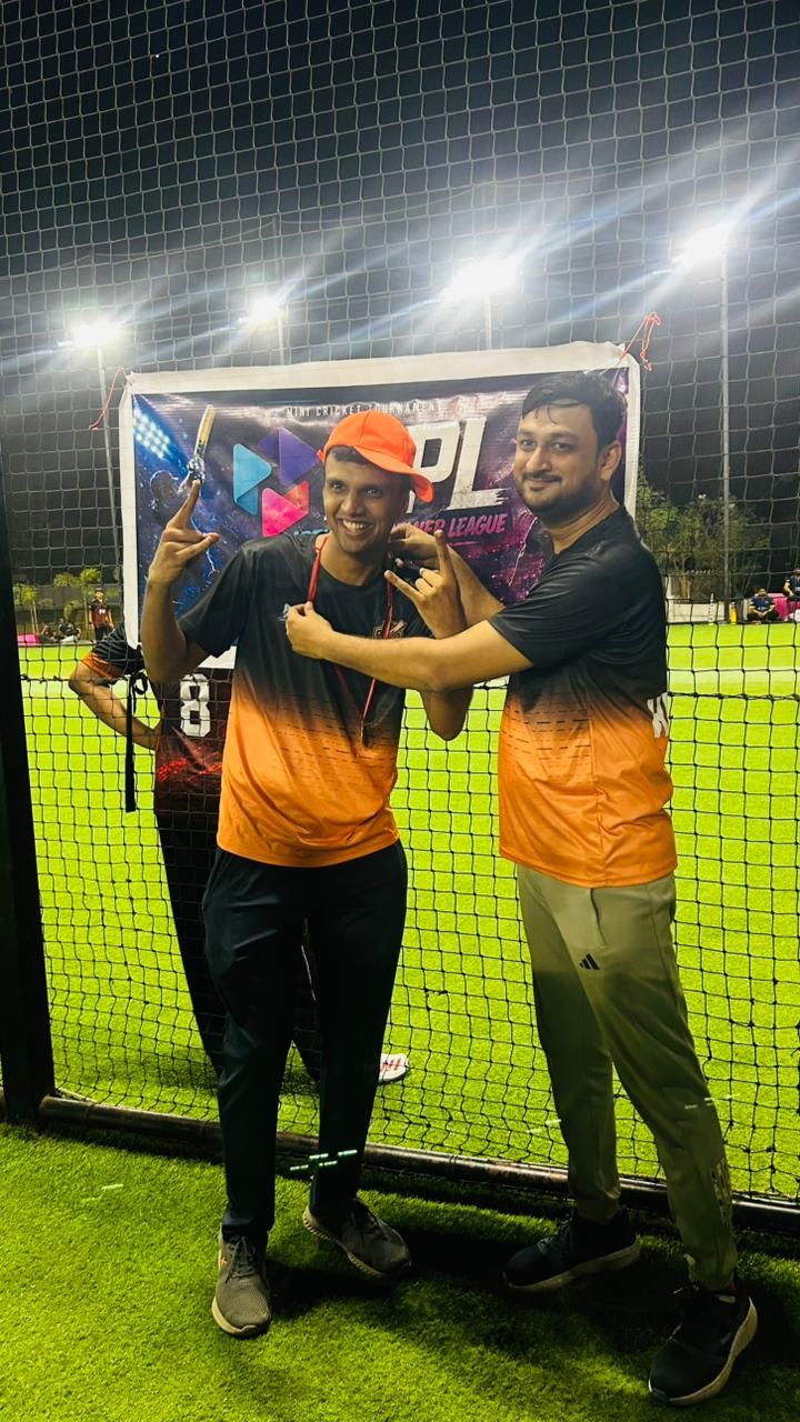 Two smiling men in black-and-orange jerseys pose under floodlights, one in an orange cap wearing a medal.