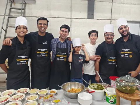 Group of people in chef hats and black aprons smile behind a table of food bowls at a cooking event.