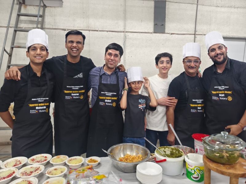 Group of people in chef hats and black aprons smile behind a table of food bowls at a cooking event.