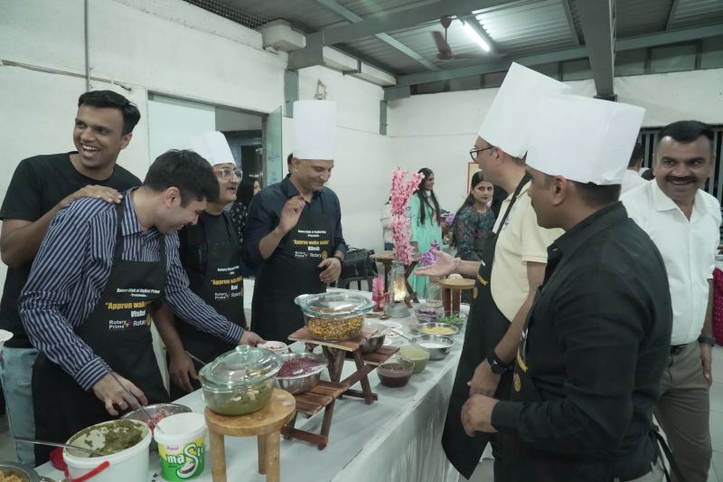 People in chef hats serve dishes and chat around a buffet counter during a cooking event.