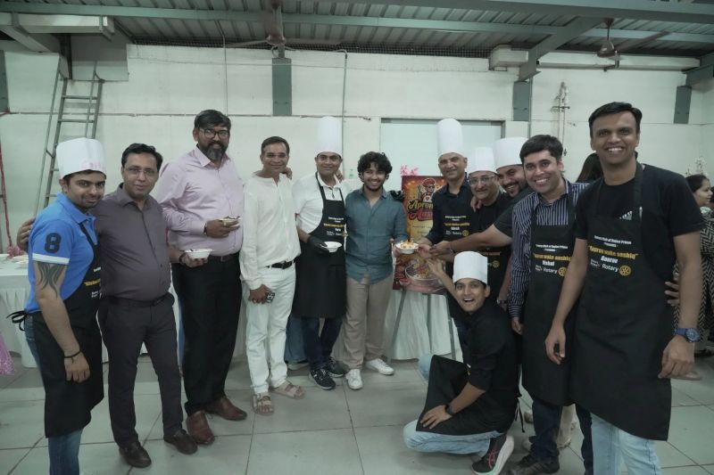 Group of men, some in chef hats and aprons, pose indoors near a poster at a cooking event.