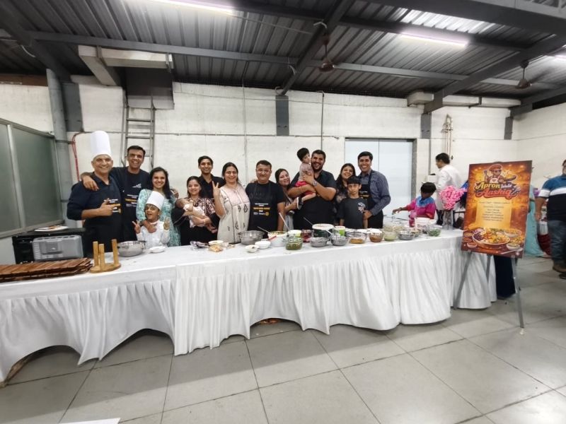Large group of adults and children behind a long buffet table of dishes beside an event poster.