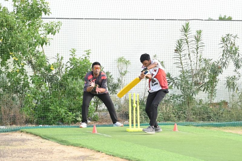 A batsman swings a yellow bat at the stumps during net practice as a wicketkeeper crouches behind.