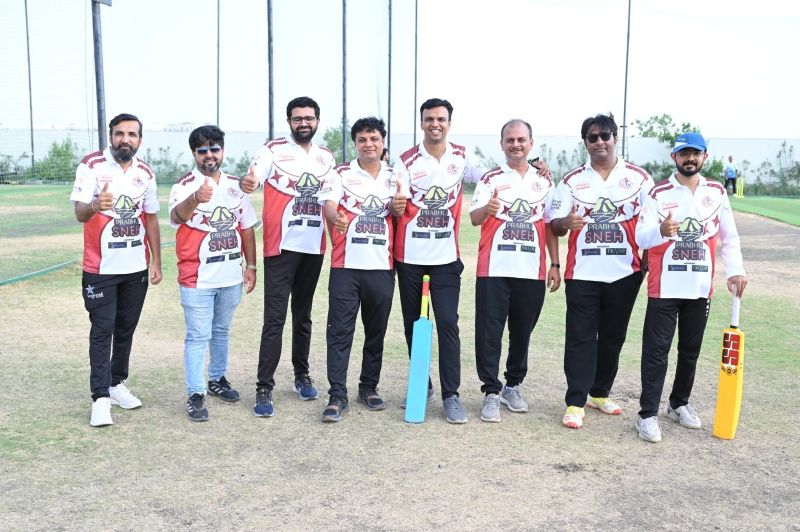 Nine men in matching white cricket jerseys give thumbs-up on a field, two of them holding bats.