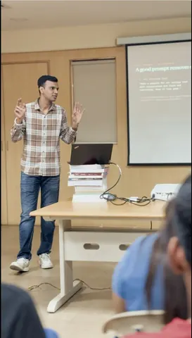 Gaurav gestures with both hands while presenting to a seated audience in front of a projector slide.