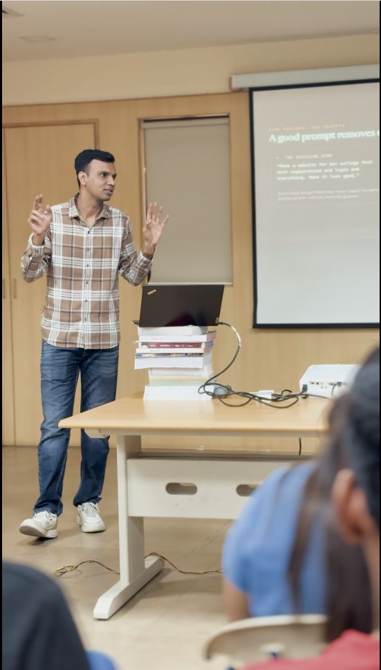 Gaurav gestures with both hands while presenting to a seated audience in front of a projector slide.