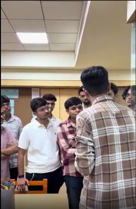 A small group of students talk with a man in a plaid shirt in a hallway after the talk.